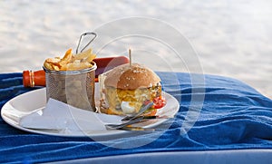 Classic beef burger with cheese and french fries. on white plate. Fast food on the beach. Blue background. Selective focus