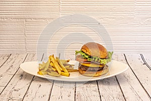 Classic beef burger with red onion, tomato slices, cheddar cheese and iceberg lettuce on a white tray and a side of French fries