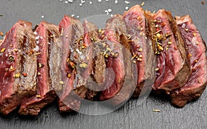 Classic beef steak uncooked meat fried outside, red inside with red juice, cut into pieces on a black board