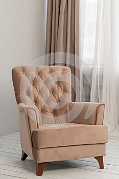 A classic beige armchair stands in the room near the window. Curtains and tulle hang behind it. Modern and elegant interior design