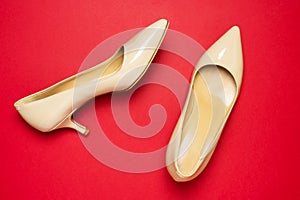Classic beige patent leather pumps or shoes with low kitten heels on red background