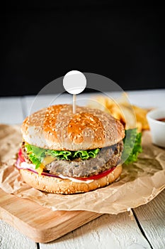 Classic big hamburger with beef, sauce and french fries on dark background. American tasty food. White frame