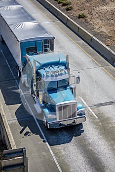 Classic big rig blue semi truck tractor transporting cargo in bulk semi trailer with covered top driving on the  elevated road