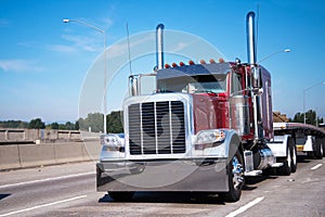 Classic big rig semi truck in dark red and flat bed semi trailer