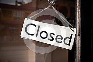 Classic black and white sign and chain hangs on an angle in a glass storefront or door due to the shop or retail business being