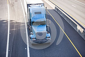 Classic blue big rig bonnet semi truck transporting cargo in refrigerator semi trailer moving on wide road