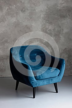 Classic blue velvet art deco armchair with wooden legs against a gray wall. Front view. Soft selective focus