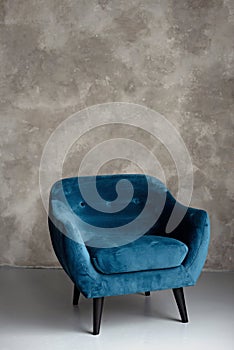 Classic blue velvet art deco armchair with wooden legs against a gray wall. Front view. Soft selective focus