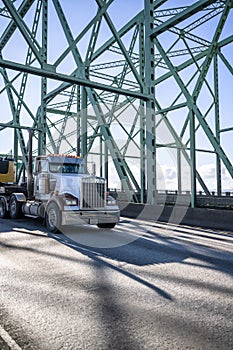 Classic bonnet big rig diesel semi truck transporting equipment on flat bed semi trailer running on Columbia River Interstate