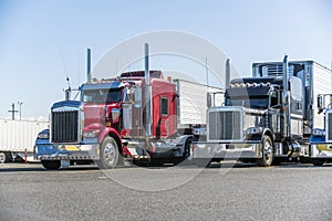 Classic bonnet big rigs semi trucks with reefer semi trailers standing in row on truck stop parking lot waiting for delivery