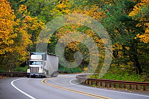 Classic bonneted semi truck ribbed trailer on road autumn forest