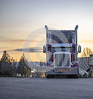 Classic burgundy big rig American semi truck tractor with high chrome pipes and refrigerator semi trailer standing for the truck