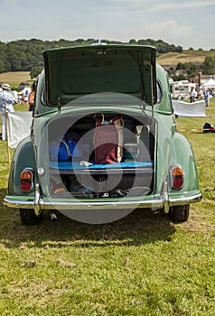 Classic car Morris Minor, parked in a field with rear boot lid (trunk lid) open displaying its contents