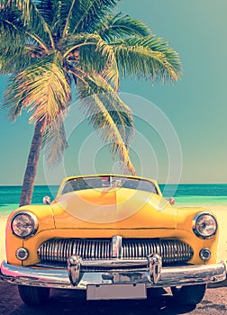 Classic car on a tropical beach with palm tree, vintage style