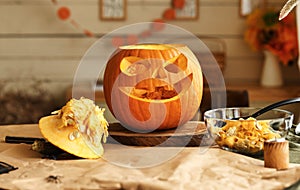 Classic carven spooky jack-o-lantern with big, gap-toothed grin on wooden table in kitchen