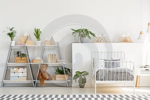 A classic child bedroom interior with simple, scandinavian style furniture and a gray wooden bookcase with a teddy bear