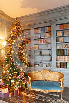 Classic Christmas New Year decorated interior room home library with fireplace. Christmas tree with gold ornament decorations.