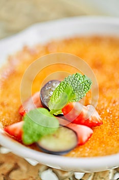 Classic creme brulee in glass bowl. Appetizing ice cream close up. Delicious dessert with grape and strawberry Sugary