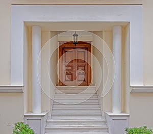 A classic design house entrance with columns, private portico and marble stairs to a natural wood door.