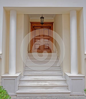 A classic design house entrance with columns, private portico and marble stairs to a natural wood door.