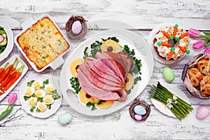 Classic Easter ham dinner. Top down view table scene on a white wood background.