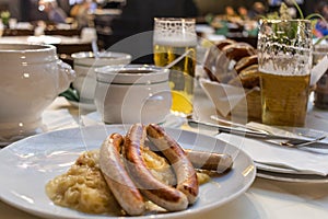 Classic German dinner of fried sausages with braised cabbage on large white plates with light beer, standing on table in