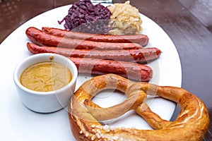 Classic German snacks, sausages with mustard cabbage and bagel on a white plate