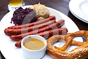 Classic German snacks, sausages with mustard cabbage and bagel on a white plate