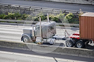 Classic gray bonnet American big rig semi truck transporting container on flat bed semi trailer moving fast on the multilevel