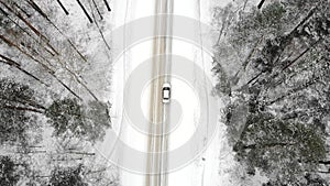 Classic gray car driving through the white winter snowy forest on country road. Top view. Winter or alpine road in the