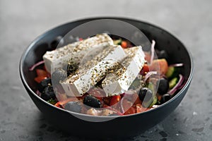 Classic greek salad in black bowl on concrete background