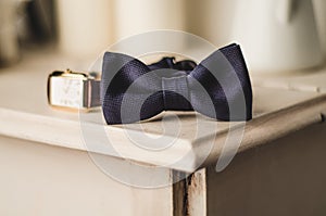 Classic groom accessories: blue bow tie and watch on a wooden table. Set of men's stylish vintage clothing. Male