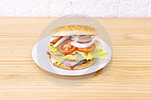 Classic hamburger with a lot of tomato, a lot of white onion, iceberg lettuce, ham and a slice of cheese on a beef fillet