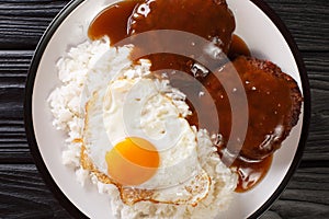 Classic Hawaiian dish, Loco Moco consists of steamed rice with juicy hamburger steak, fried egg and gravy close-up on a plate.