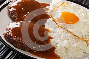 Classic Hawaiian dish, Loco Moco consists of steamed rice with juicy hamburger steak, fried egg and gravy close-up on a plate.