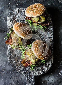 Classic homemade burger with pork cutlet, bacon, pickles, fried onions and mayonnaise mustard sauce on wooden chopping board, on