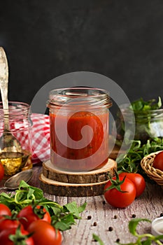 Classic homemade tomato sauce for pasta and pizza in a glass jar on a board. Composition with herbs, spices and tomatoes.