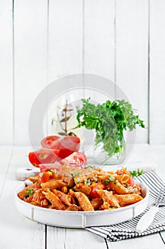 Classic italian pasta penne arrabbiata with vegetables on white wooden table.