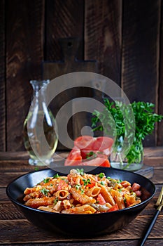 Classic italian pasta penne arrabbiata with vegetables on wooden table.