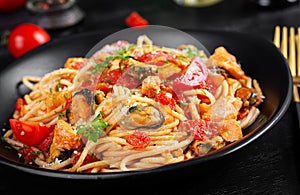 Classic italian pasta spaghetti marinara with mussels and salmon on dark table.