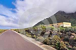 A classic landscape in a mountainous area. A small yellow house stands near the road in the mountains next to cacti