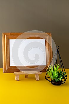 Classic landscape wooden photo frame mockup on easel beside a small houseplant, workspace decoration.
