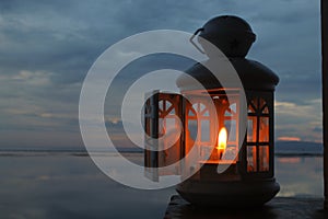 Classic lantern and candle light inside with opened window on night blue sky background at dusk in the beach.