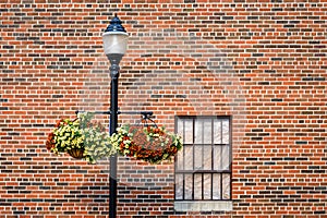 Classic light pole with hanging flower baskets against a brick wall with a bar covered window