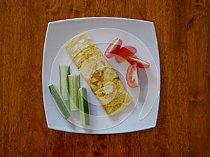 Classic omelet with tomatoes and cucumbers on the white plate.