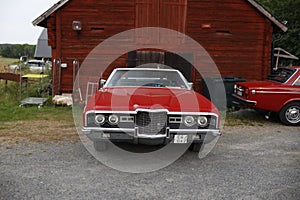 Classic Pairing: Red 1971 Ford LTD with Round Headlights and Red Volvo 142 at a Barn