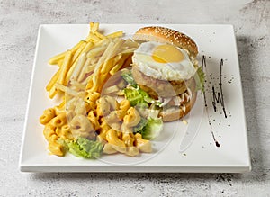 classic pork burger with sunny side up egg, mac and cheese and french fries served in dish isolated grey background top view