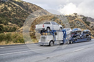 Classic powerful big rig car hauler semi truck transporting crossovers on the modular semi trailer climbing uphill on the