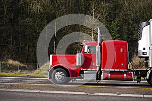 Classic powerful red big rig semi truck running on the road with