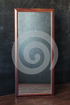 Classic rectangular mirror withot reflection standing In the empty room with black wall.